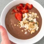 chocolate smoothie bowl topped with strawberries and shaved coconut