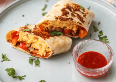High protein breakfast burrito cut in half on a plate with dipping sauce